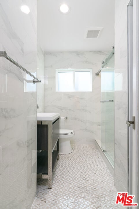 bathroom featuring vanity, toilet, walk in shower, and tile walls