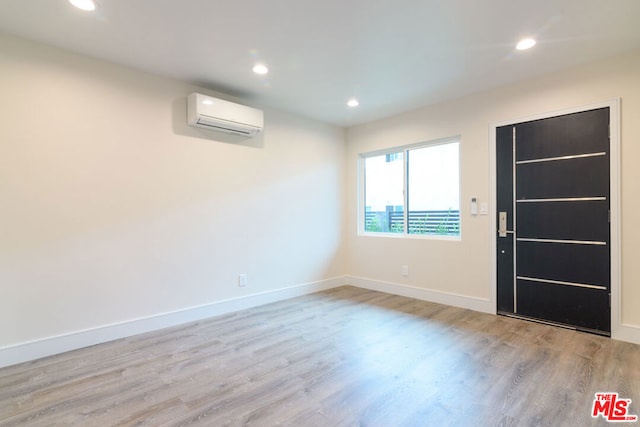 empty room with a wall mounted air conditioner and light wood-type flooring