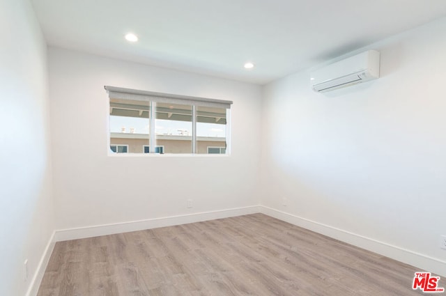 unfurnished room with a wall unit AC and light hardwood / wood-style flooring