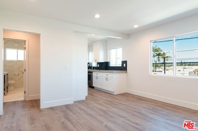 kitchen featuring stainless steel dishwasher, decorative backsplash, light wood-type flooring, and white cabinetry