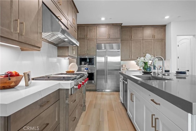 kitchen featuring built in appliances, white cabinetry, sink, and light wood-type flooring