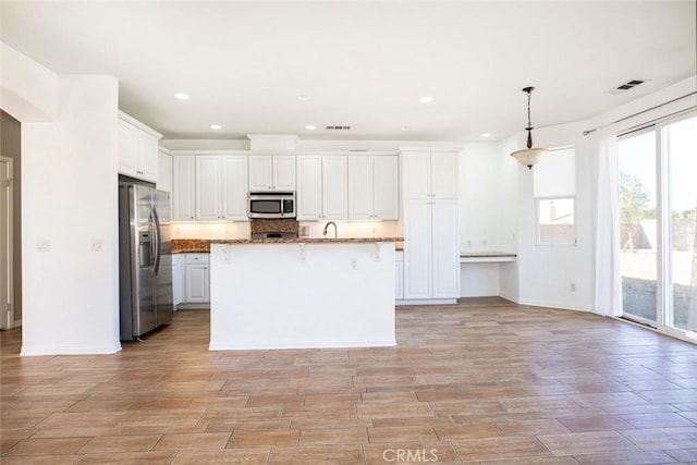 kitchen with white cabinets, pendant lighting, stainless steel appliances, and an island with sink