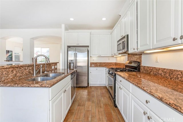 kitchen with white cabinets, appliances with stainless steel finishes, dark stone countertops, and sink