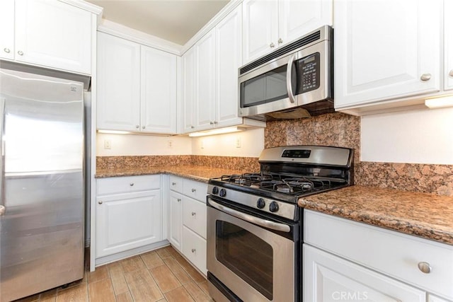 kitchen featuring dark stone countertops, light hardwood / wood-style flooring, white cabinets, and stainless steel appliances