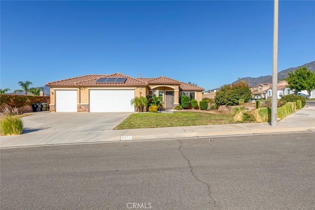 mediterranean / spanish house featuring solar panels, a garage, a mountain view, and a front yard