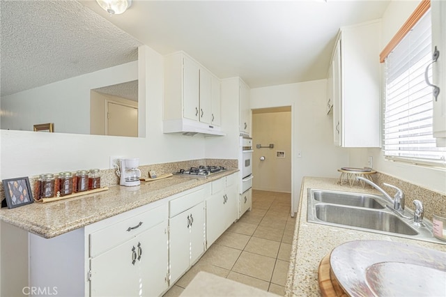 kitchen with white cabinets, light tile patterned flooring, stainless steel gas stovetop, and sink