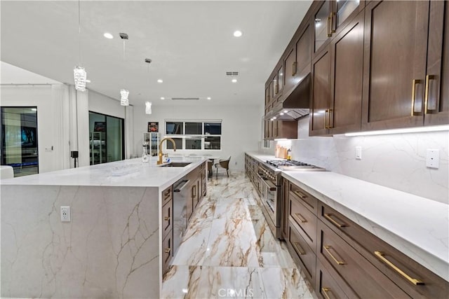 kitchen featuring a large island with sink, sink, light stone countertops, decorative light fixtures, and stainless steel appliances