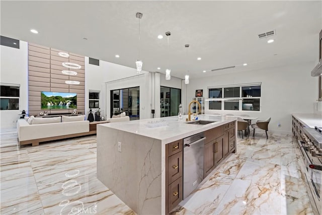 kitchen with sink, light stone counters, a large island with sink, decorative light fixtures, and appliances with stainless steel finishes