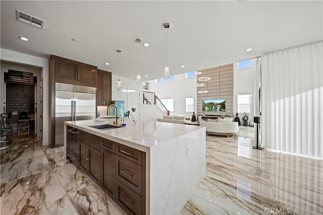 kitchen featuring a wealth of natural light, sink, hanging light fixtures, light stone counters, and an island with sink