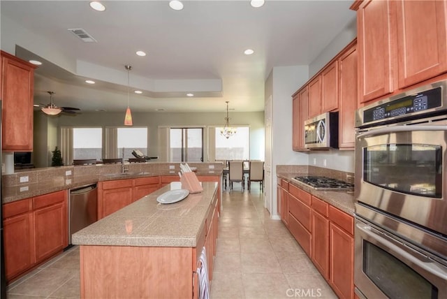 kitchen featuring ceiling fan with notable chandelier, stainless steel appliances, sink, decorative light fixtures, and a center island