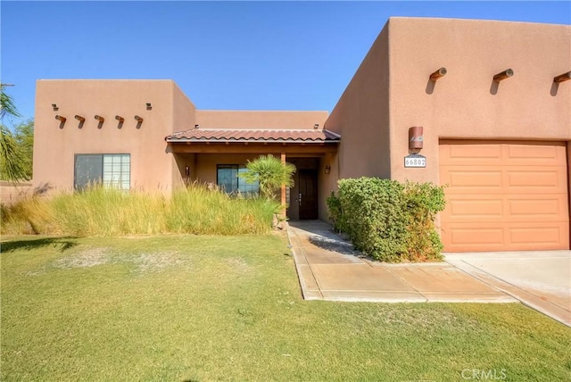 pueblo-style home featuring a front yard and a garage