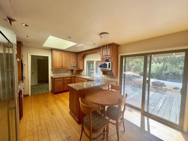 kitchen featuring a skylight, kitchen peninsula, tasteful backsplash, pendant lighting, and sink