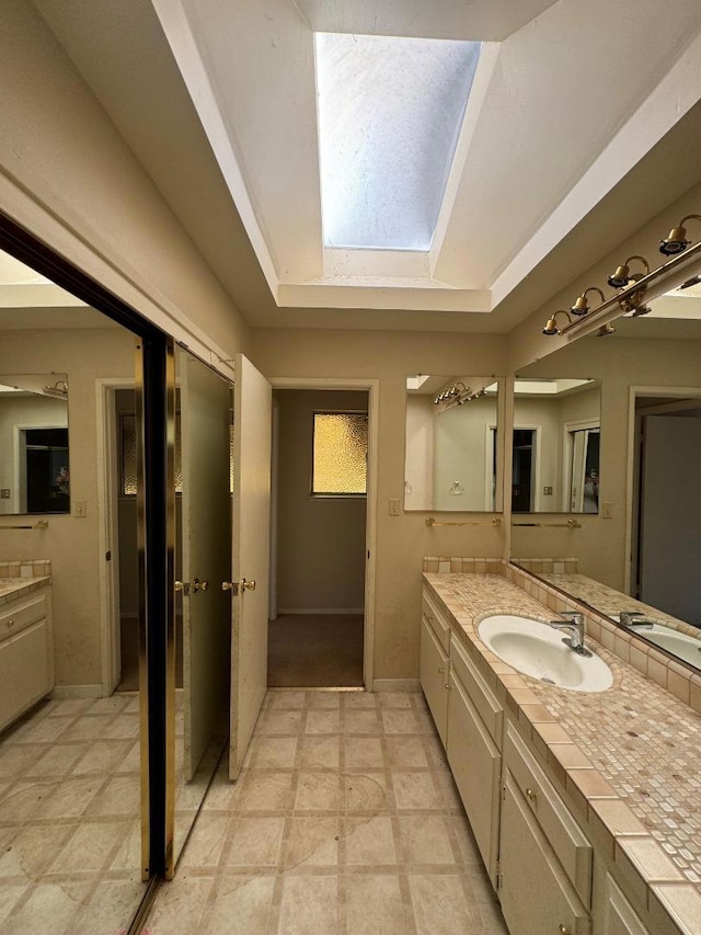 bathroom with a tray ceiling, vanity, and a skylight