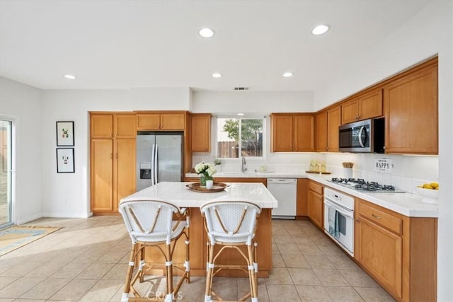 kitchen with light tile patterned flooring, sink, a kitchen island, a kitchen bar, and stainless steel appliances