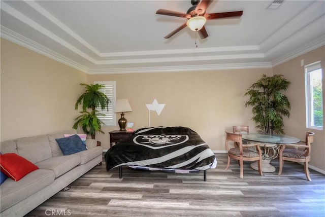 living room featuring wood-type flooring, a raised ceiling, and crown molding