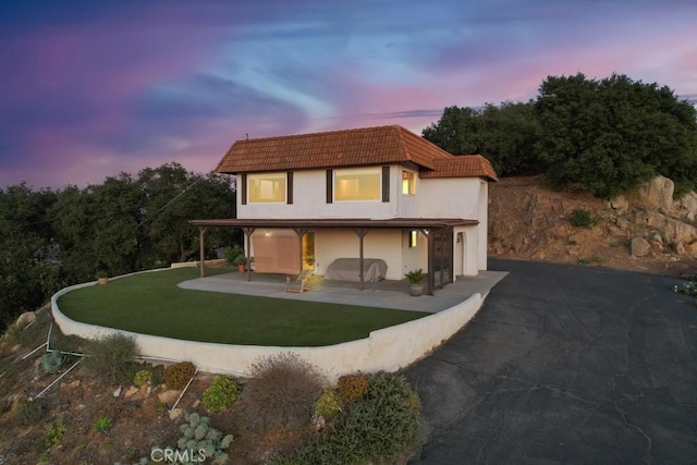 back house at dusk featuring a yard and a patio area