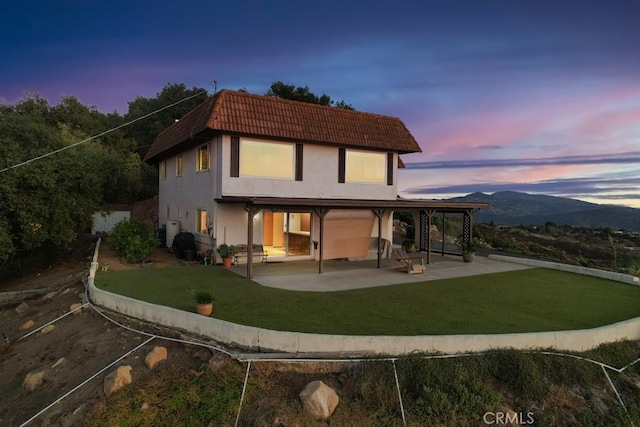 back house at dusk featuring a mountain view, a yard, and a patio