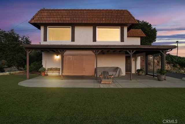 back house at dusk with a lawn and a patio area