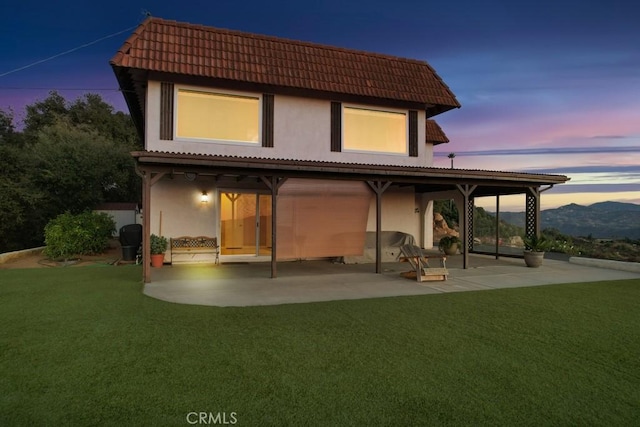 back house at dusk featuring a lawn, a patio area, and a mountain view