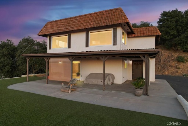 back house at dusk with a lawn and a patio area