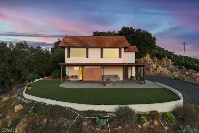 back house at dusk with a lawn and a patio area