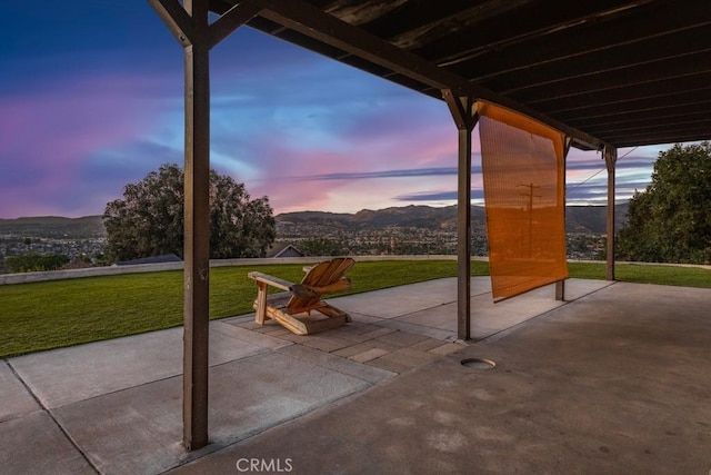 patio terrace at dusk featuring a lawn and a mountain view