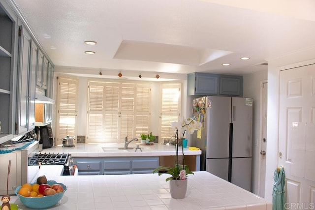 kitchen featuring sink, a tray ceiling, stainless steel refrigerator, and tile countertops