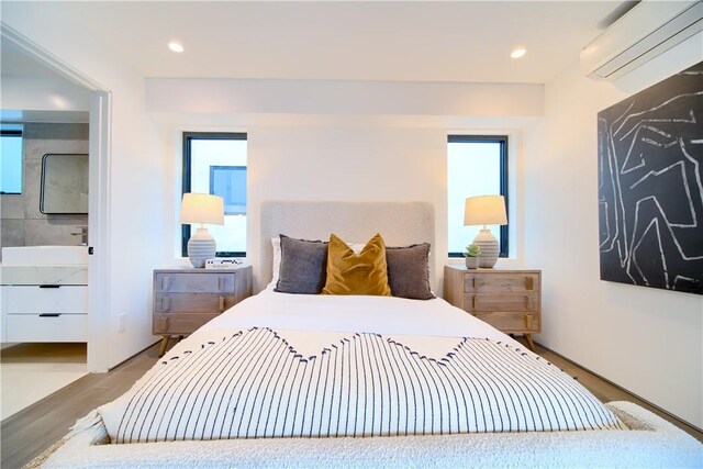 bedroom with a wall unit AC, connected bathroom, sink, and light wood-type flooring