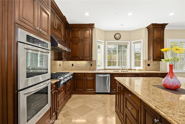 kitchen featuring appliances with stainless steel finishes, extractor fan, light stone counters, and backsplash