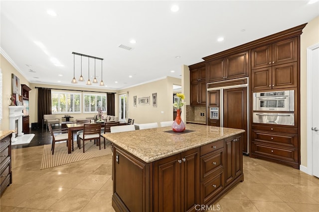 kitchen with stainless steel oven, a kitchen island, ornamental molding, paneled built in fridge, and decorative light fixtures