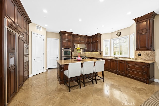 kitchen with backsplash, double oven, a center island, extractor fan, and a breakfast bar area