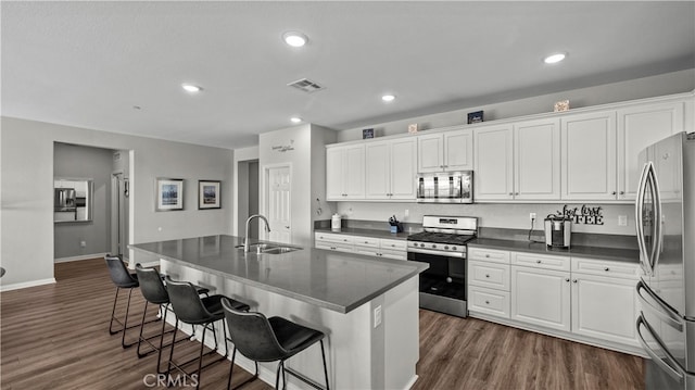 kitchen featuring dark wood-type flooring, an island with sink, stainless steel appliances, sink, and white cabinetry