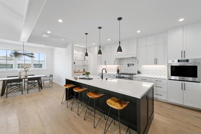 kitchen with appliances with stainless steel finishes, white cabinetry, a kitchen island with sink, and light hardwood / wood-style floors