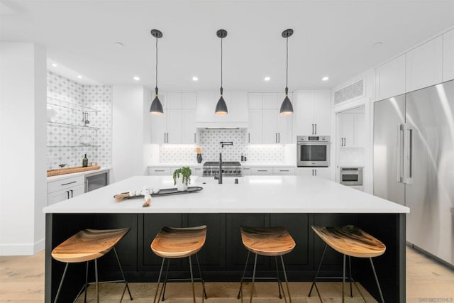 kitchen with appliances with stainless steel finishes, tasteful backsplash, light wood-type flooring, and an island with sink