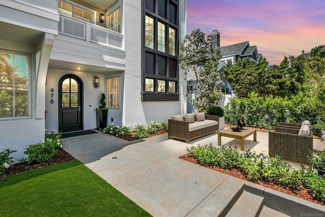 exterior entry at dusk with a patio, outdoor lounge area, and a balcony