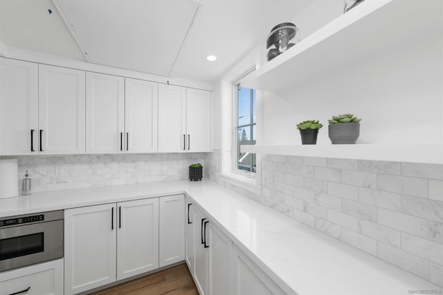 kitchen with oven, white cabinets, tasteful backsplash, dark hardwood / wood-style floors, and light stone counters