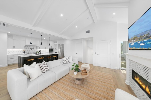 living room featuring beamed ceiling, light hardwood / wood-style flooring, a fireplace, and high vaulted ceiling