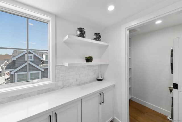 bar with light stone countertops, decorative backsplash, white cabinets, and wood-type flooring