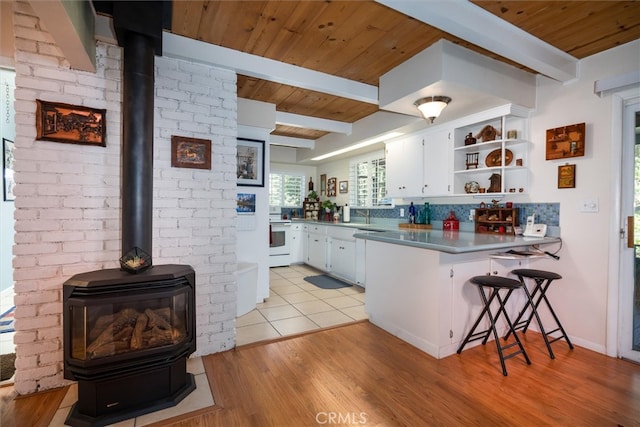 kitchen with kitchen peninsula, white cabinetry, light wood-type flooring, white stove, and a wood stove