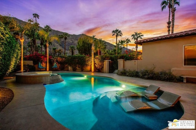 pool at dusk featuring an in ground hot tub, a mountain view, and a patio