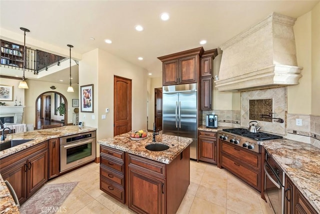 kitchen featuring custom exhaust hood, stainless steel appliances, decorative backsplash, a high end fireplace, and sink