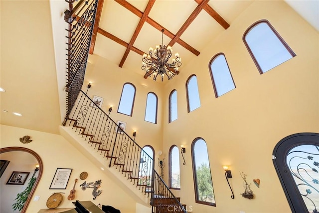 stairway with beam ceiling, a high ceiling, an inviting chandelier, and coffered ceiling