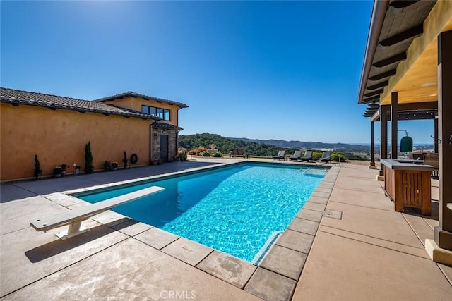 view of pool with a diving board, a patio area, and a mountain view