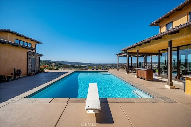 view of swimming pool with a mountain view, a patio area, and a diving board