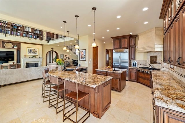 kitchen with a large island with sink, premium range hood, pendant lighting, sink, and appliances with stainless steel finishes