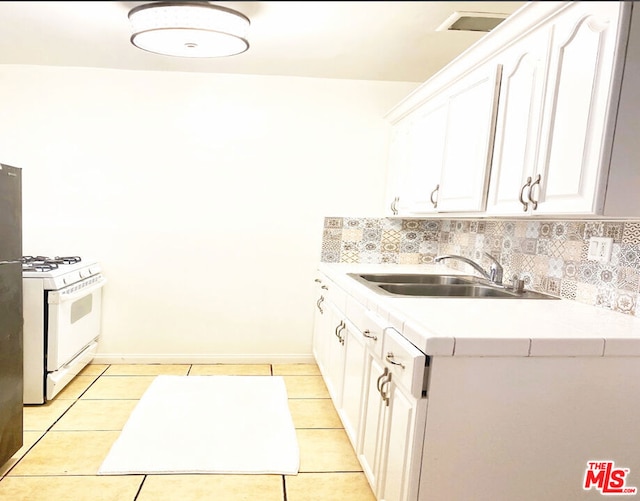 kitchen with decorative backsplash, sink, light tile patterned floors, white range with gas stovetop, and white cabinetry