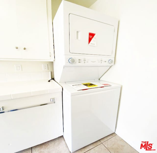 clothes washing area featuring light tile patterned flooring, cabinets, and stacked washer and clothes dryer