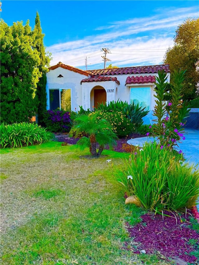 mediterranean / spanish house with a tile roof, stucco siding, and a front lawn