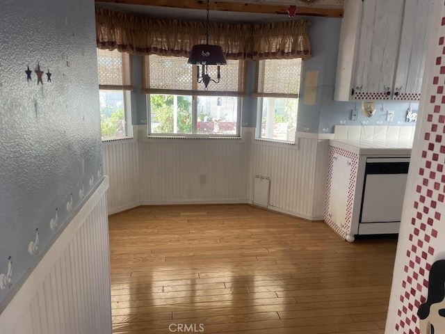 kitchen featuring pendant lighting, dishwasher, light hardwood / wood-style floors, and wooden walls