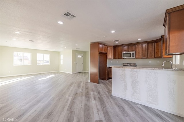 kitchen with sink, light stone countertops, light wood-type flooring, a textured ceiling, and appliances with stainless steel finishes